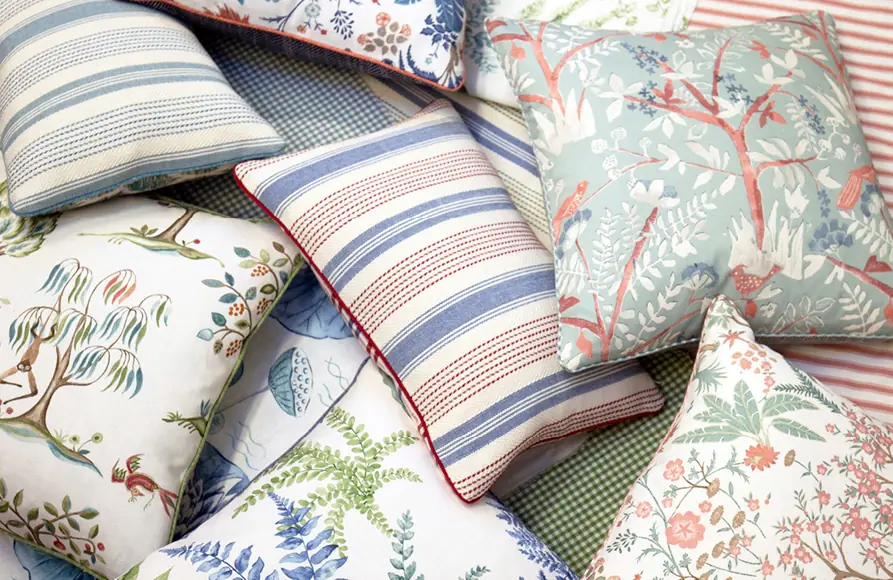 Stapel bedrukte kussens in rood, groen en blauw. Stoffen van Baker Lifestyle.