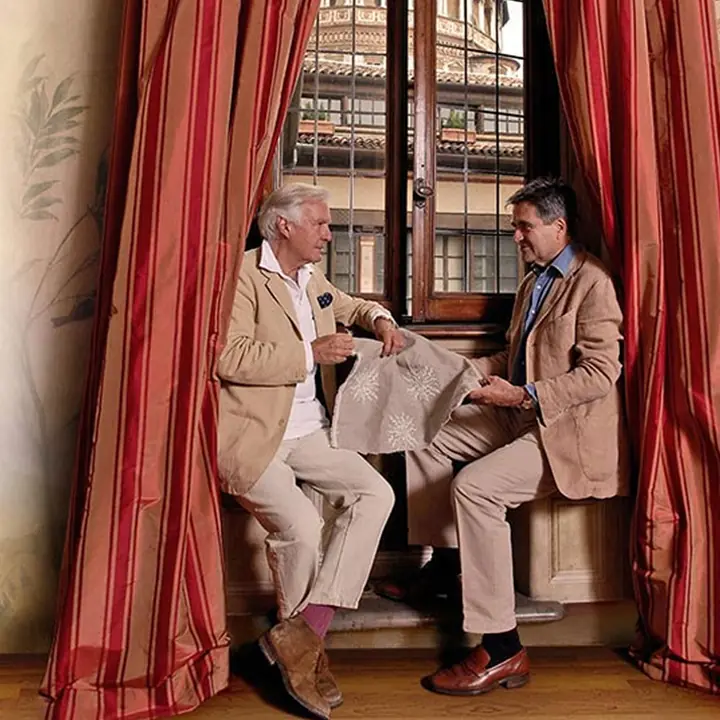 Twee mannen met stof bij rode gordijnen. Stoffen van C&C Milano.