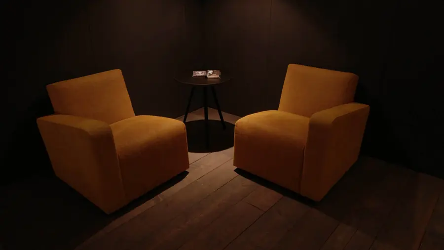 Twee okergele fauteuils in een donkere ruimte. Meubelen van Corneille & Silence.
