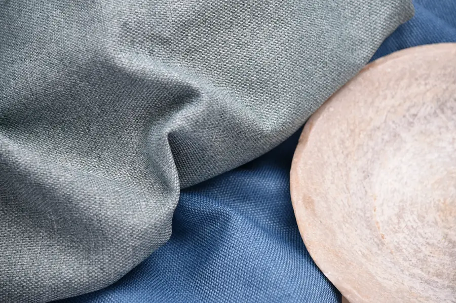 Gordijnstof in blauw en grijs bij een houten schaal. Stoffen van Indetex.
