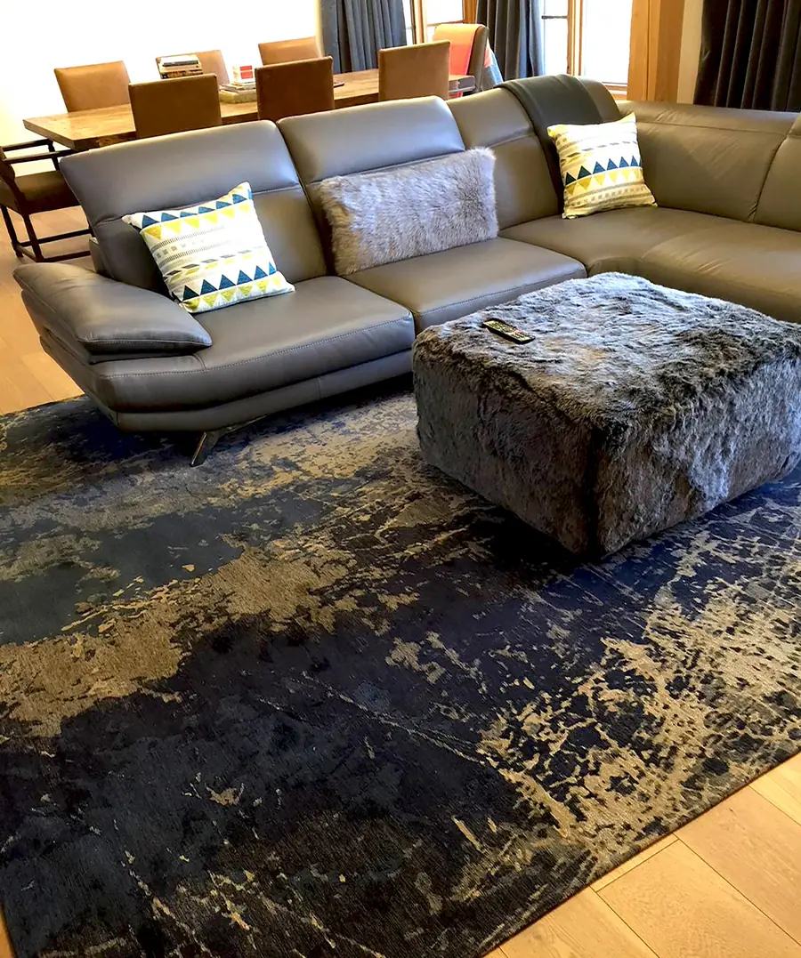 Blauwgoud tapijt onder een lederen sofa. Tapijt van Louis De Poortere.