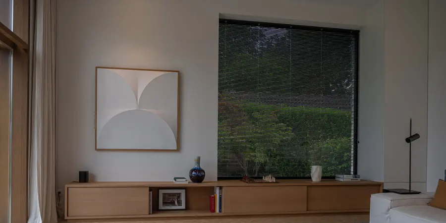 Woonkamer met horizontale jaloezie voor groen raam. Zonwering van Louverdrape.