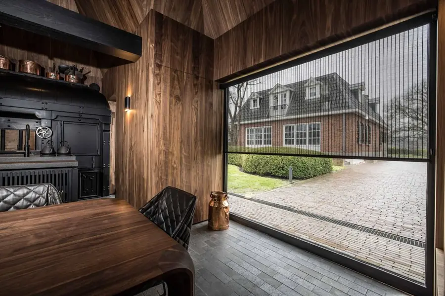 Eetkamer met bamboe rolgordijn voor een groot raam. Zonwering van Nature Deco.