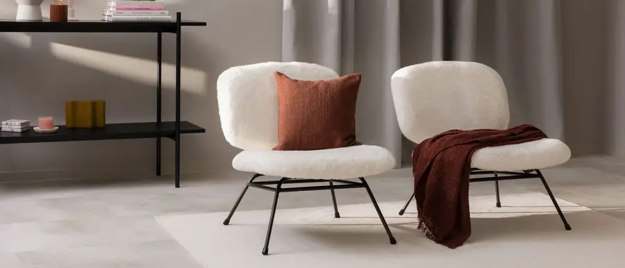 Twee witte fauteuils in boucle met kussens in terracotta. Stoffen van Symphony Mills.