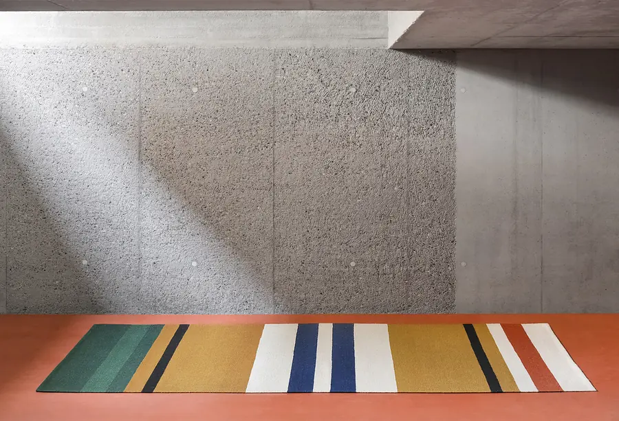 Gestreept tapijt op een betonvloer. Bedtextiel van The Alfred Collection.