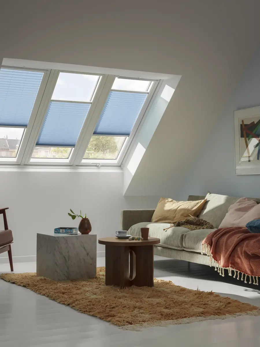 Woonkamer met blauwe plisségordijnen voor de dakramen. Raamdecoratie van Velux.