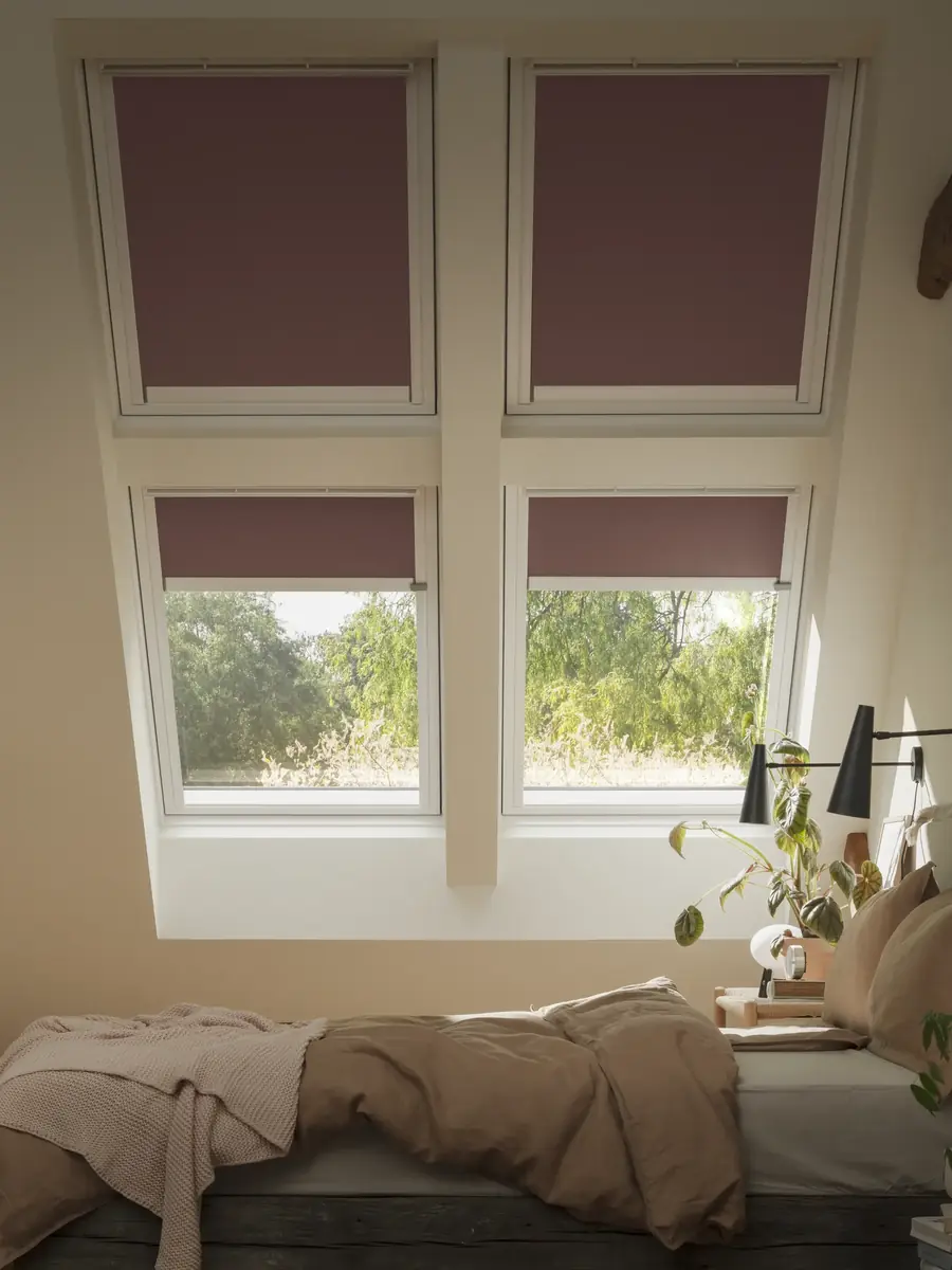 Bordeaux rolgordijnen voor twee dakramen boven een werkhoek. Raamdecoratie van Velux.